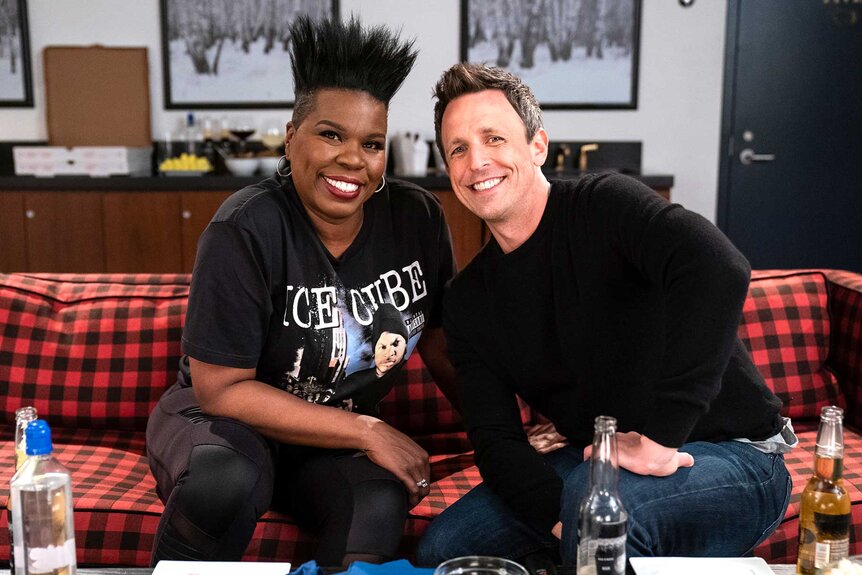 Leslie Jones and Seth Meyers smiling and posing together on a plaid couch.