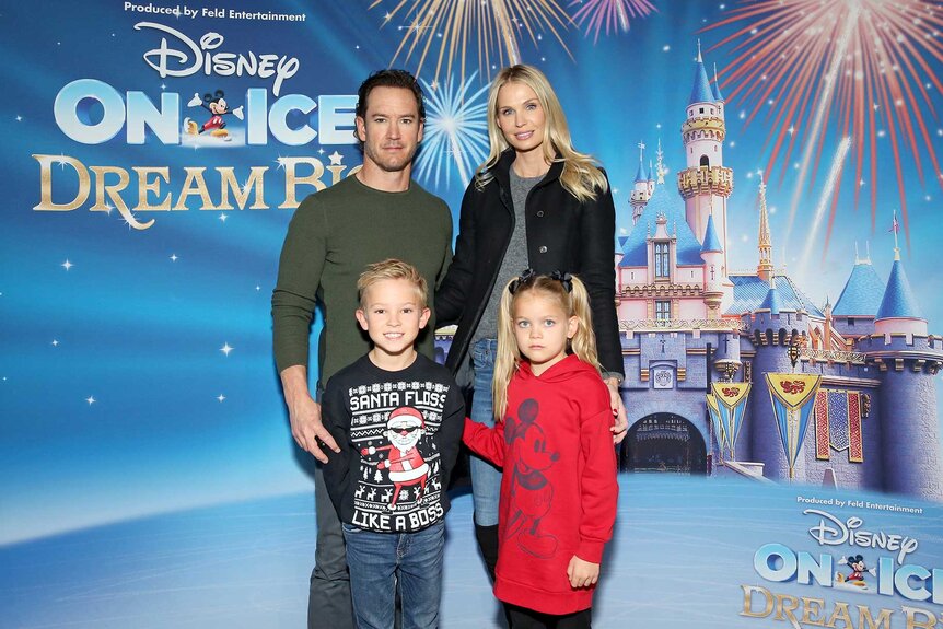 Mark-Paul Gosselaar, Catriona McGinn and their children posing in front of a Disney On Ice sign.
