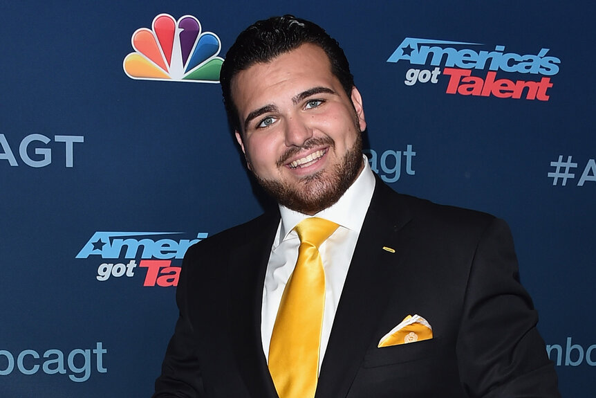 Sal Valentinetti smiles wearing a suit with a yellow tie