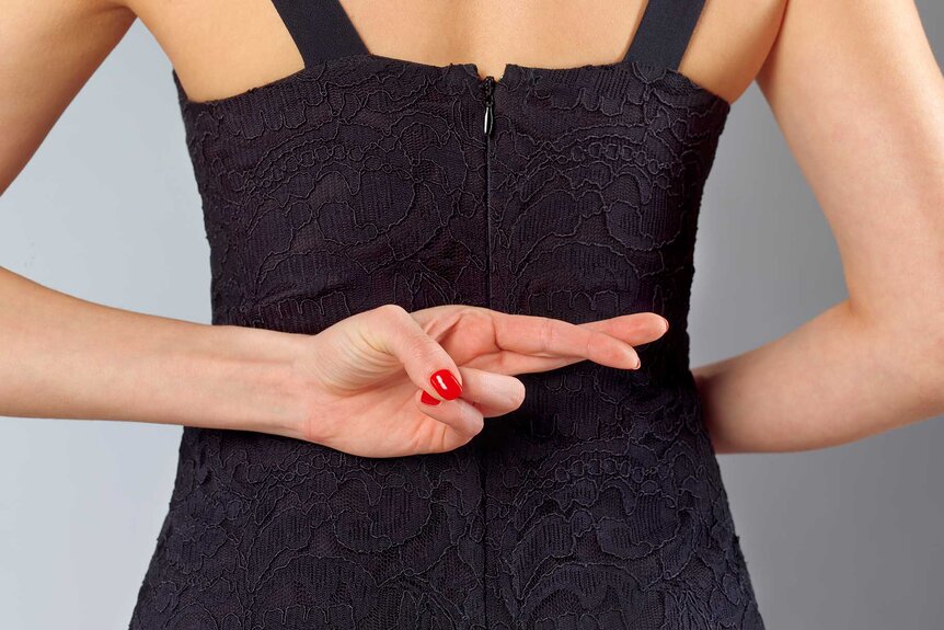 A woman in a black dress crossing her fingers behind her back.