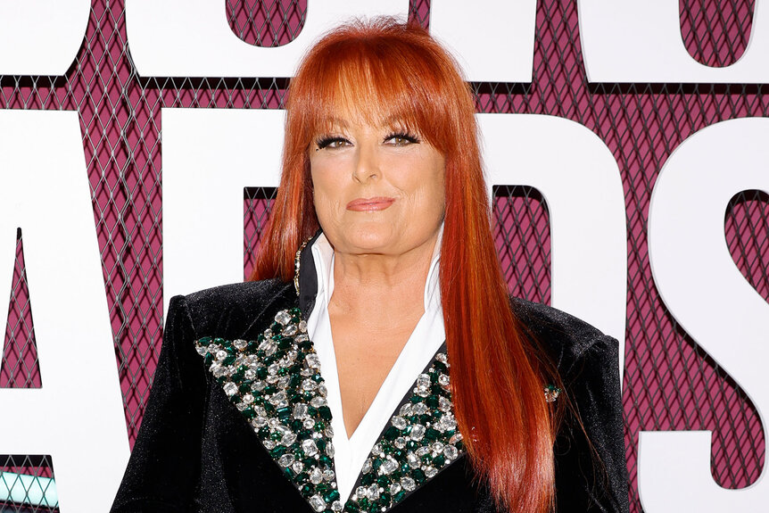 Wynonna Judd wears a black blazer and smiles on the red carpet during the CMT Music Awards