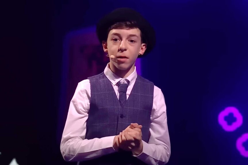 Cillian O'Connor, wearing a suit vest and tie, standing on stage with his hands together.