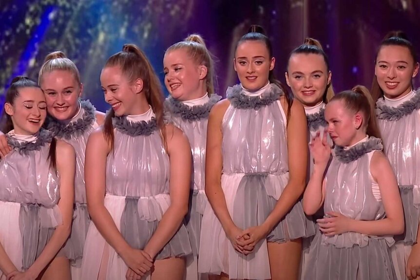 Mersey Girls in silver glittery outfits standing next to each other in a group on stage.