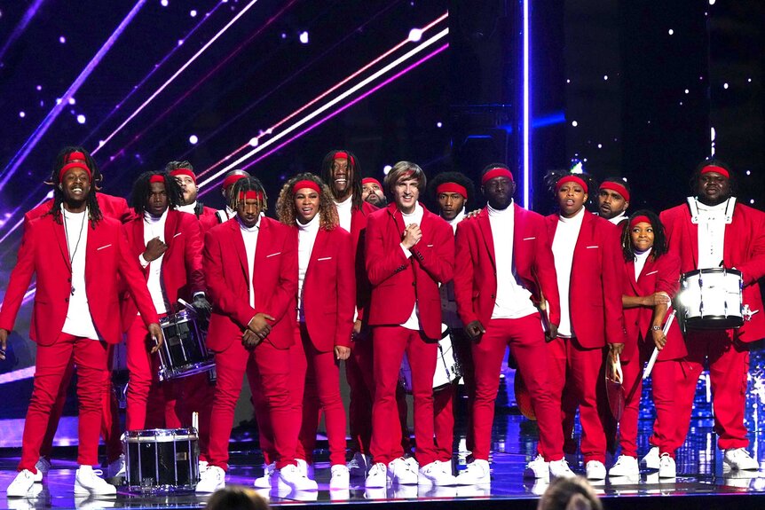 The Pack Drumline, wearing all red outfits, standing together on stage in a group.