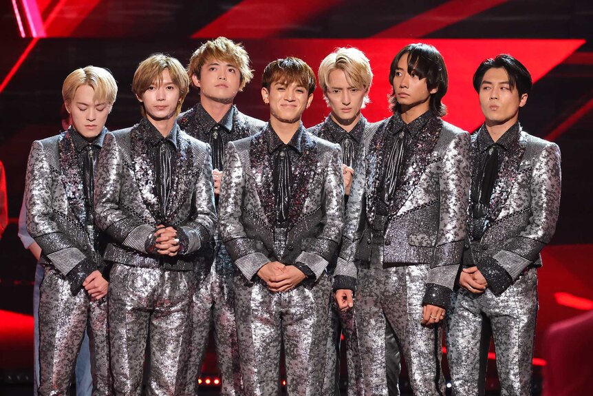Travis Japan, wearing silver suits, grouped together on stage.