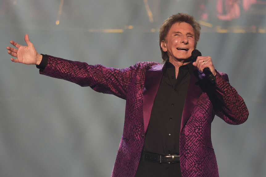 Barry Manilow outstretches his arm as he performs onstage