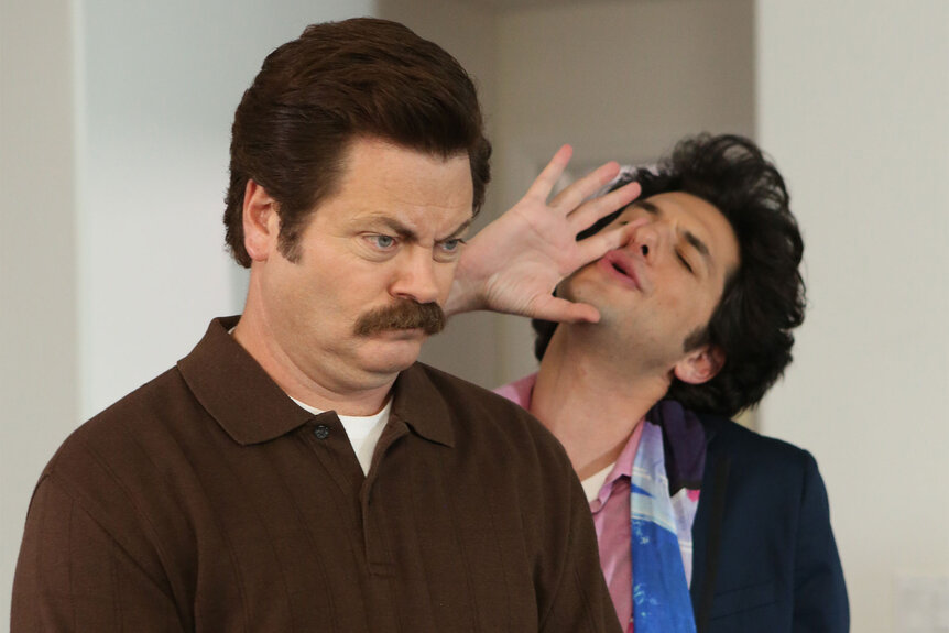 Nick Offerman as Ron Swanson stands in front of and Ben Schwartz who speaks into his ear