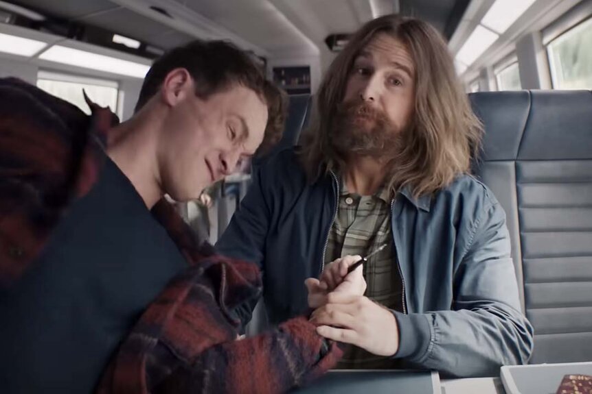 Sam Rockwell twists the arm of a man with a pen in his hand on a train in Argylle (2024).