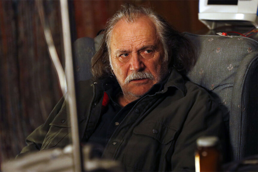 Rade Serbedzija as Bogdan Krilov sits in a chair looking solemn