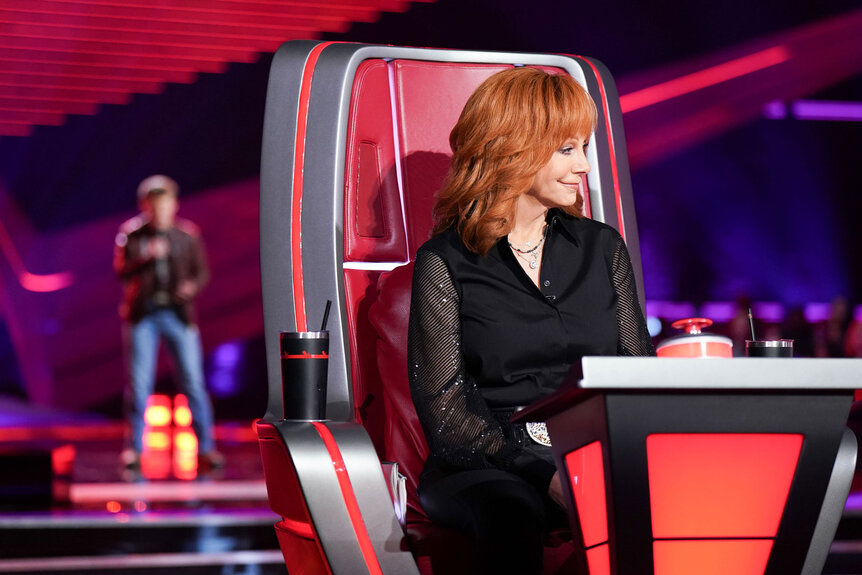 Reba McEntire sits in her chair and listens to a performer