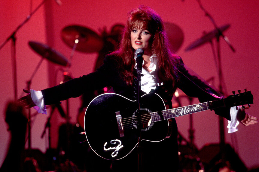 Wynonna Judd outstretches her arms while performing onstage