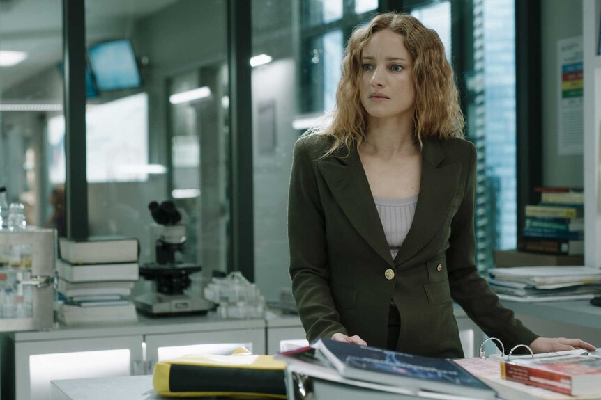 Dr. Magalie Leblanc, wearing an olive green blazer, standing over a desk with books.