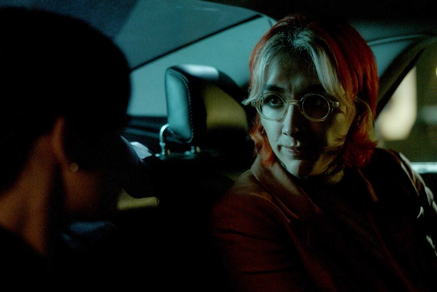 A close-up of Ian looking at another character while in a car at night.