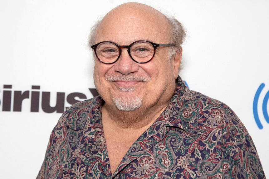 Danny Devito smiles wearing glasses at an event