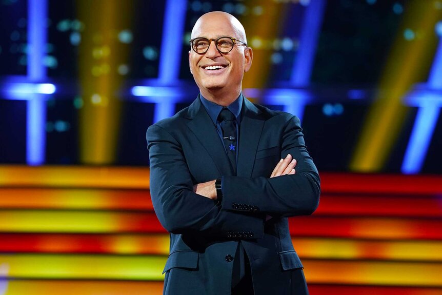 Howie Mandel smiling with his arms crossed on the set of Deal or No Deal.