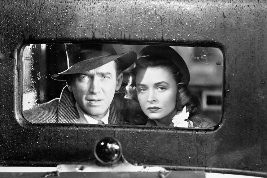 James Stewart and Donna Reed look out of the back window of vintage car