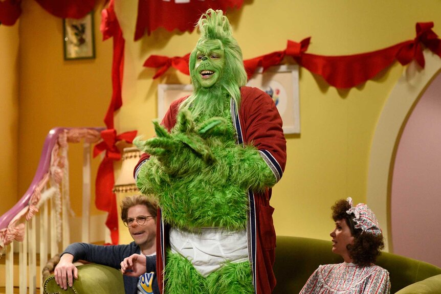 Pete Davidson dressed as the Grinch with two people sitting in the background on the set of Saturday Night Live.