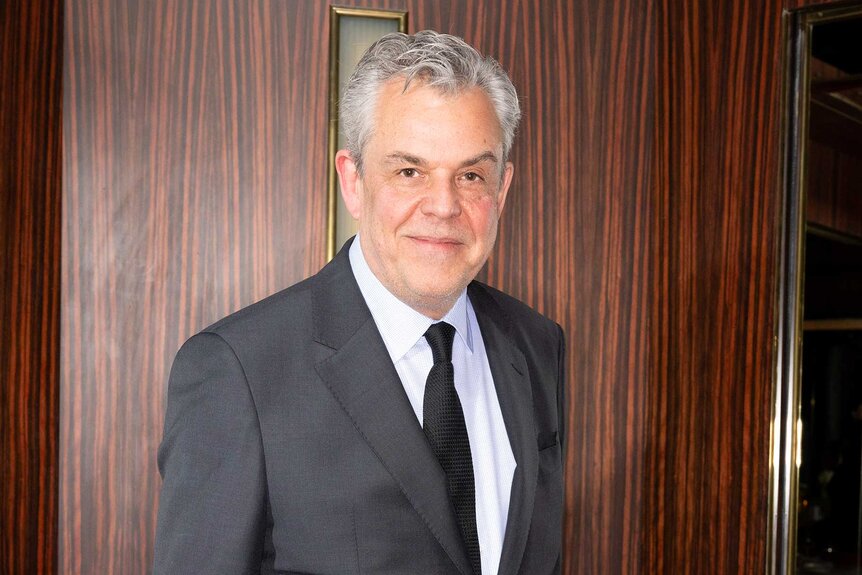 A close up of Danny Huston wearing a gray suit.