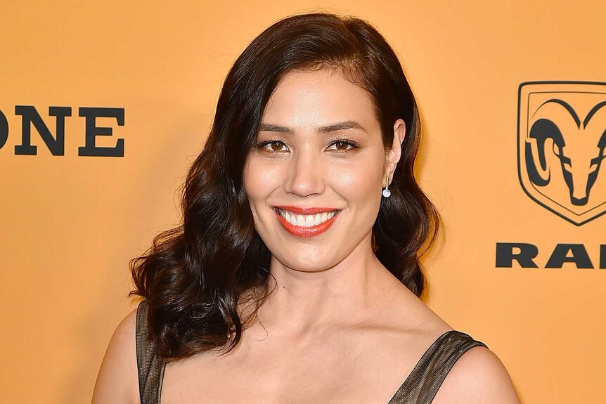 A close up Michaela Conlin smiling in front of an orange backdrop.
