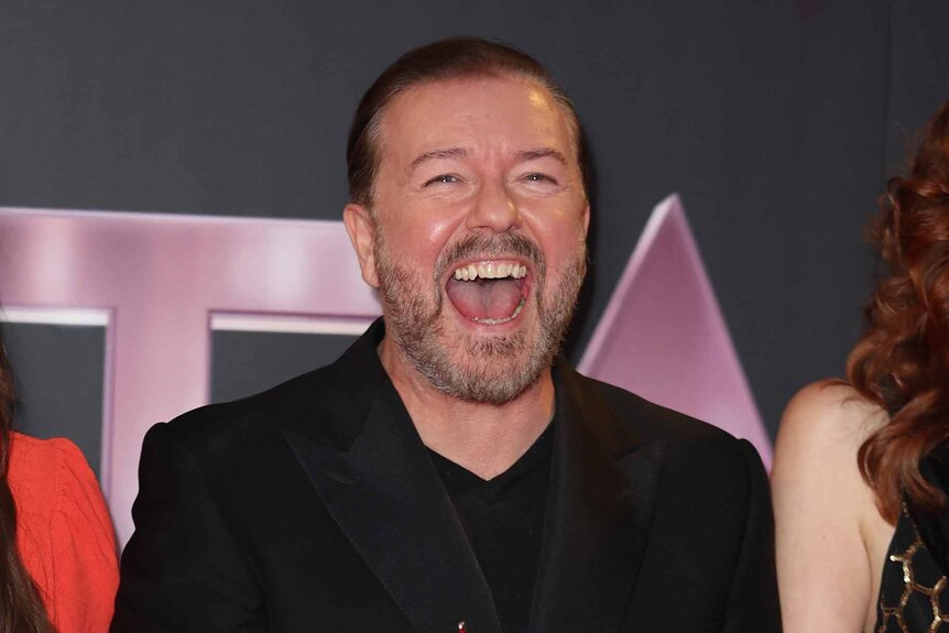 Ricky Gervais smiles wide while wearing all black