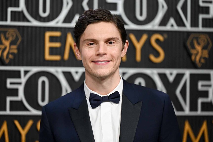 Evan Peters smiles in a suit and bowtie.
