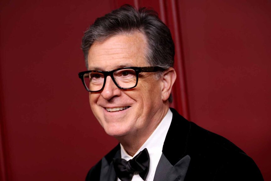 Stephen Colbert smiles in a suit and bowtie.