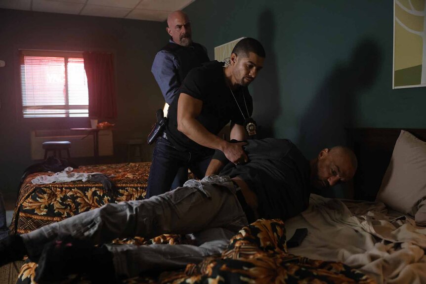 Det. Elliot Stabler and Det. Bobby Reyes detain and handcuff Miguel "Mig" Espinosa on a motel bed in Law & Order: Organized Crime 401.