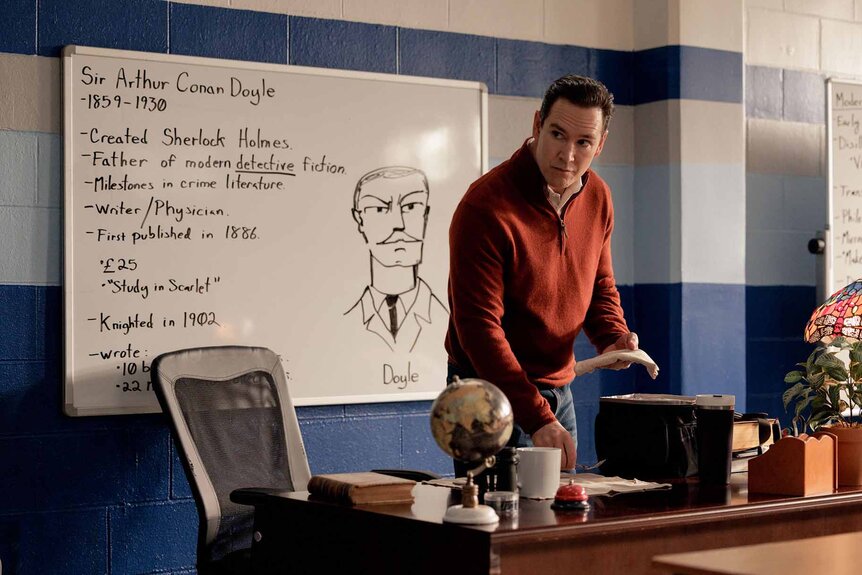 Sir stands at a desk in front of a whiteboard in Found Episode 113.