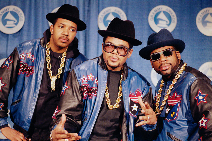 Run RUN-DMC poses in heavy gold chains, hats, sunglasses, and Adidas track suits