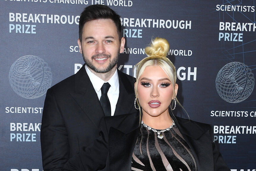 Matt Rutler holds Christina Aguilera at the hips both wearing black on the red carpet for the 9th Annual Breakthrough Prize Ceremony