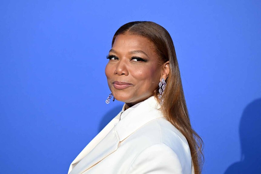 Queen Latifah swears a white suit in front of a blue background.