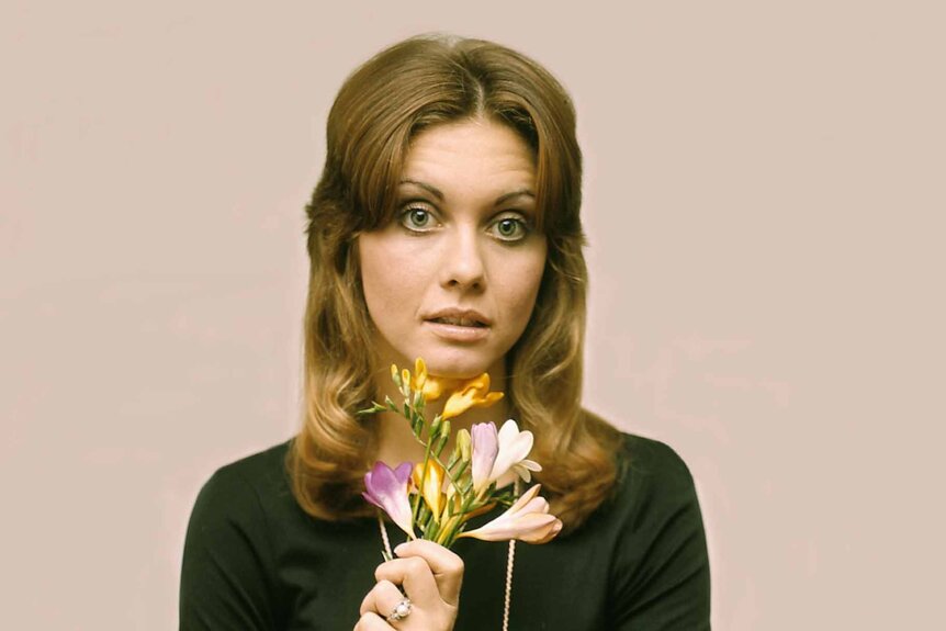 Olivia Newton-John poses with a bunch of flowers.