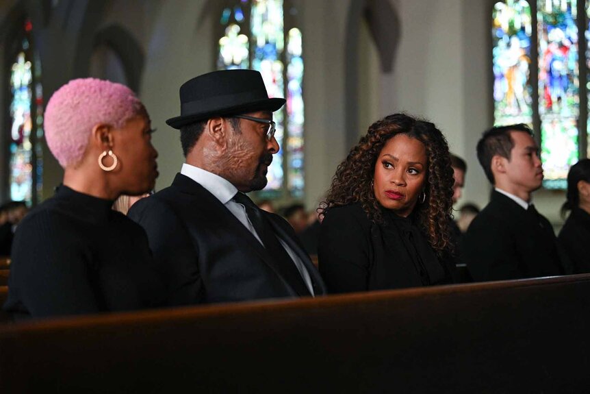 Kylie, Alec Mercer, and Marisa are dressed in all black and sitting in a church pew in The Irrational Episode 111.