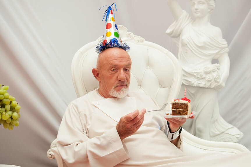 Professor Hickey (Jonathan Banks) eats birthday cake while wearing a white robe and birthday hat