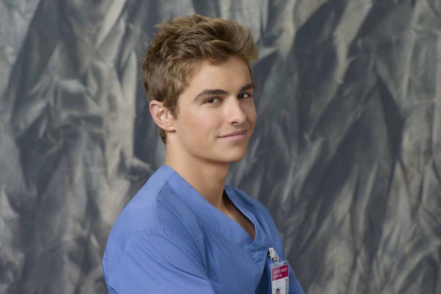 Cole Aaronson (Dave Franco) stands in front of a grey background in Scrubs.
