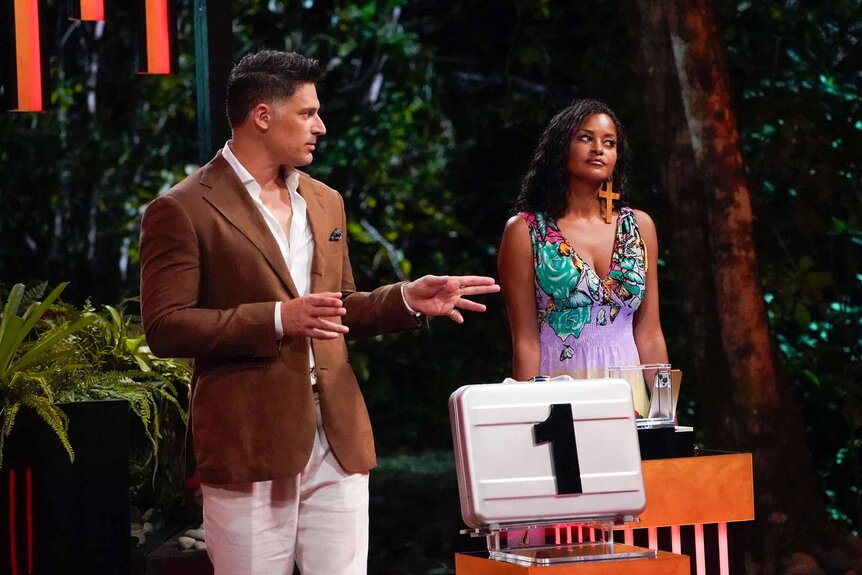 Claudia Jordan and Joe Manganiello stand near a briefcase labeled '1' on Deal or No Deal Island Episode 103