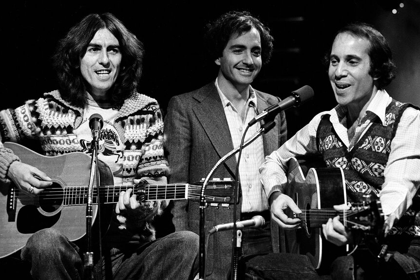 Paul Simon and George Harrison perform with Lorne Michaels on Saturday Night Live on November 20, 1976.