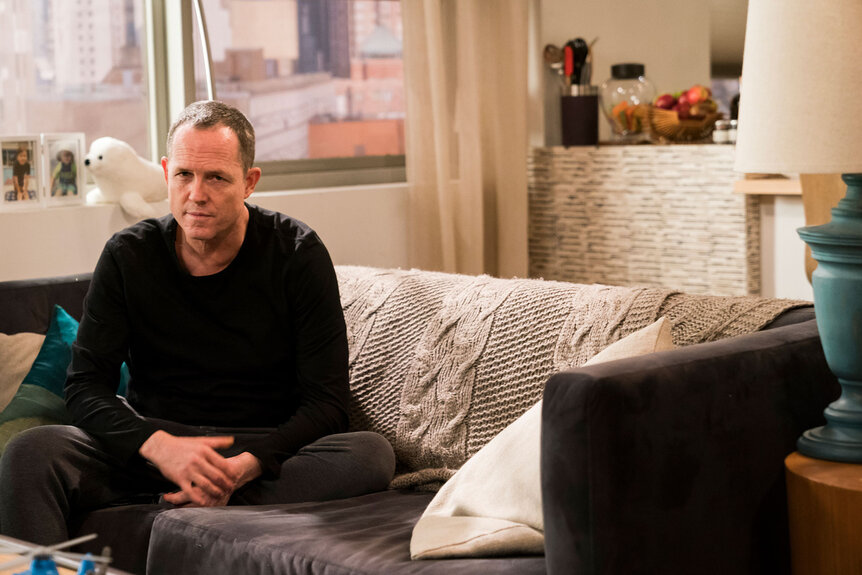 Detective Brian Cassidy (Dean Winters) sits on a couch in Law & Order: Special Victims Unit Season 19 Episode 14.